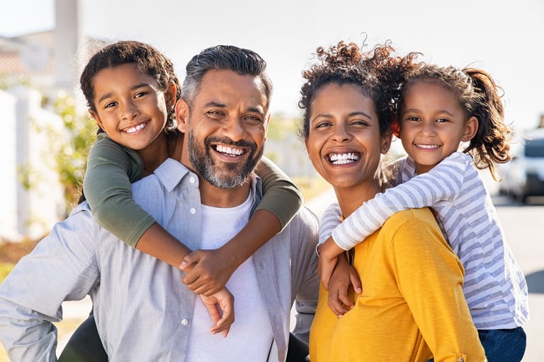 Happy family of four smiling outdoors in casual clothing on a sunny day